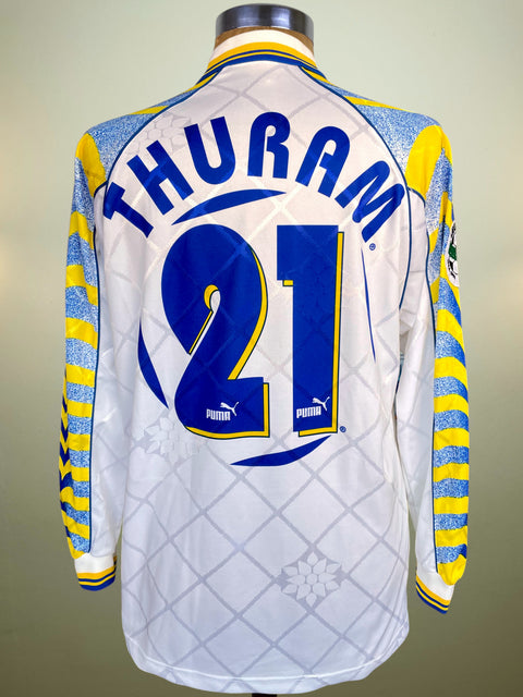 White sports jersey with blue and yellow accents, featuring the name 'Thuram' and number '21', on a mannequin against a neutral background.