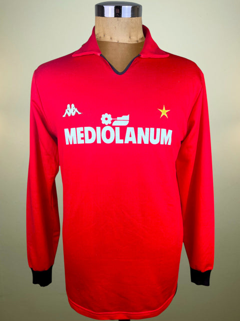 A vintage red long-sleeve Mediolanum soccer jersey by Kappa, displayed on a wooden dress form mannequin. The jersey features white printed logos and text on the chest, including the Kappa logo, a sponsor logo, a yellow star, and 'MEDIOLANUM' in bold white letters.