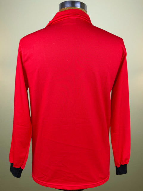 A bright red long-sleeve athletic top shown from the back on a mannequin, with black cuffs at the wrists, against a plain light beige background.