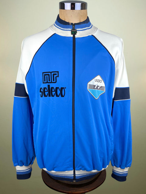 Blue and white Lazio training jacket from the 1982-83 season made by Ennerre with Seleco Sponsor with logos on a mannequin against a beige background