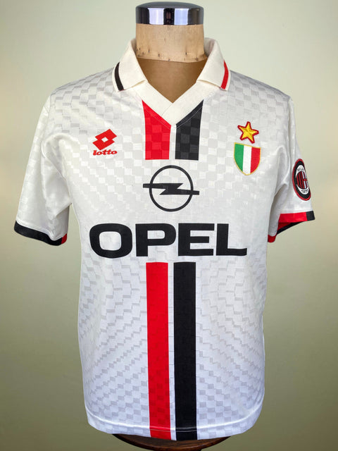 A vintage AC Milan soccer jersey by Lotto, featuring a white textured pattern with red and black vertical stripes, displayed on a wooden mannequin torso against a neutral beige background.