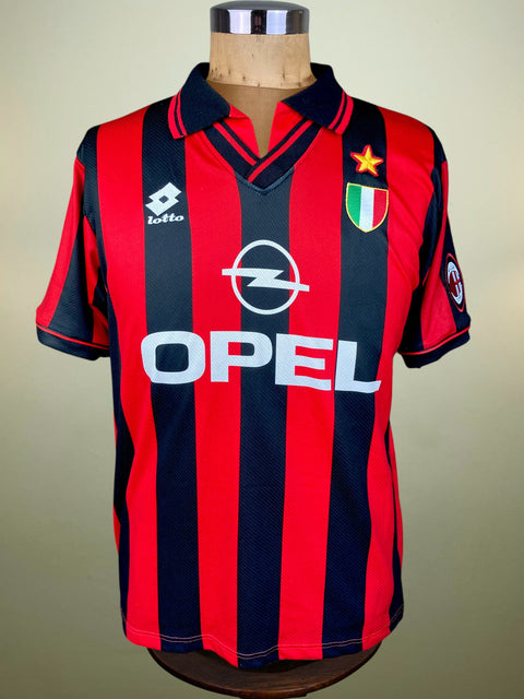 A vintage AC Milan soccer jersey by Lotto, featuring red and navy blue vertical stripes with the Opel logo and Italian crest, displayed on a wooden mannequin torso.