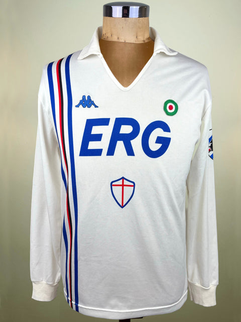 A vintage white long-sleeve soccer jersey by Kappa, featuring blue 'ERG' lettering across the chest, a blue Kappa logo, and a red, white, and blue vertical stripe on the right side. The jersey is displayed on a wooden mannequin torso against a neutral beige background.