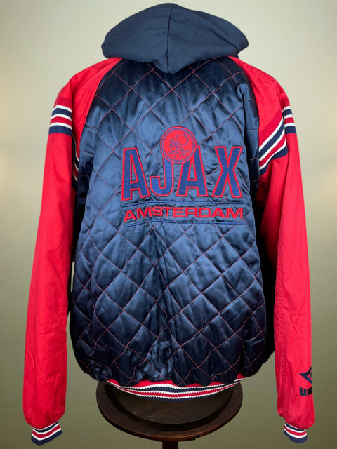 A red and navy blue Ajax Amsterdam jacket with a quilted navy back panel, red sleeves, and a navy hood, displayed on a stand.