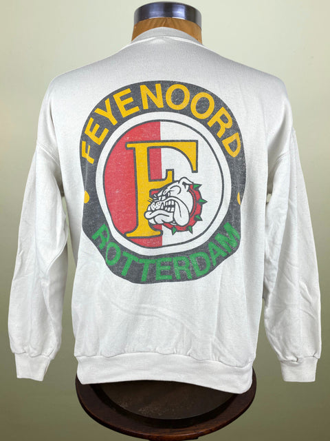 A white long-sleeve Sweatshirt displayed on a mannequin torso, showing the back with a large vintage-style circular graphic. The design features a yellow 'F' with a bulldog mascot inside a red and white circle, bordered by yellow 'FEYENOORD' text at the top and green 'ROTTERDAM' text at the bottom.