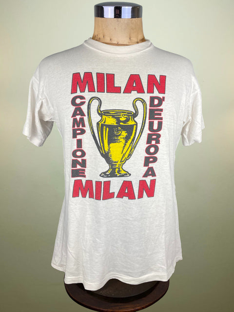 White t-shirt with 'Milan Campione d'Europa' text and trophy graphic on a mannequin against a beige background