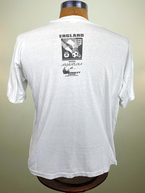 A white short-sleeve t-shirt displayed on a wooden dress form, showing the back side with a black graphic print featuring the text 'ENGLAND' and a soccer-themed design.