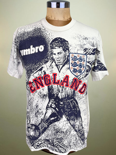 A vintage Umbro England soccer t-shirt displayed on a wooden mannequin torso. The white short-sleeve t-shirt features a distressed black graphic of a soccer player, the England crest, and 'ENGLAND' printed in red arched text across the chest.