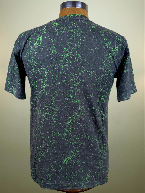 A short-sleeve t-shirt displayed on a mannequin from the back, featuring a dark charcoal gray base with a vibrant green splatter or tie-dye pattern.
