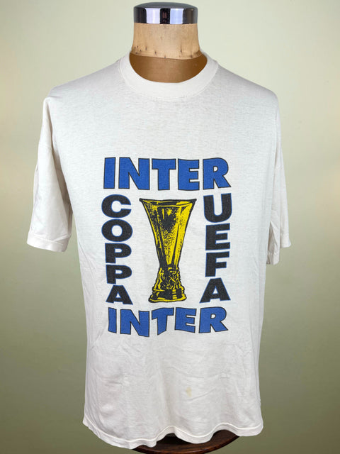 A vintage white short-sleeve t-shirt displayed on a wooden mannequin torso. The shirt features a large graphic print celebrating the Inter Coppa UEFA final, with 'INTER COPPA INTER' and 'UEFA' printed in blue and black, flanking a yellow trophy illustration.