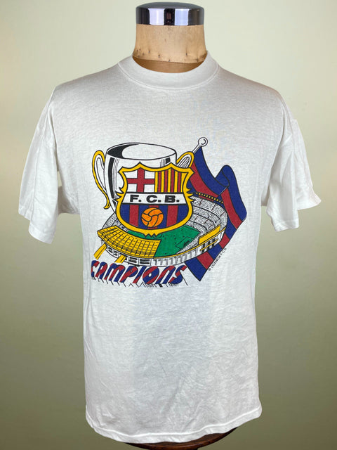 White t-shirt with Barcelona's Nou Camp Stadium and the European Cup Trophy, with the words "Campions" on a mannequin against a beige background