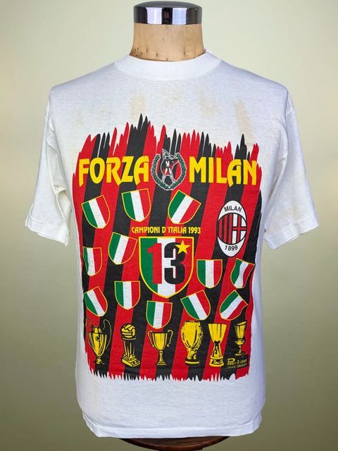 A vintage white short-sleeve t-shirt displayed on a wooden mannequin torso. The shirt features a large graphic print for the 1993 Milan football club 'Forza Milan', showcasing red and black striped background, Italian flag motifs, the number 13, and trophy illustrations.