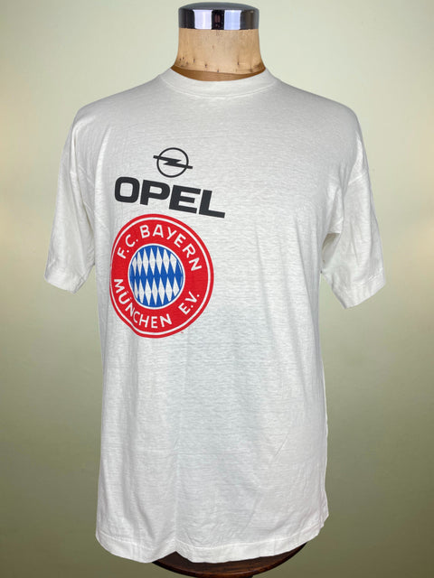 White t-shirt with Opel and FC Bayern Munich logos on a mannequin against a beige background