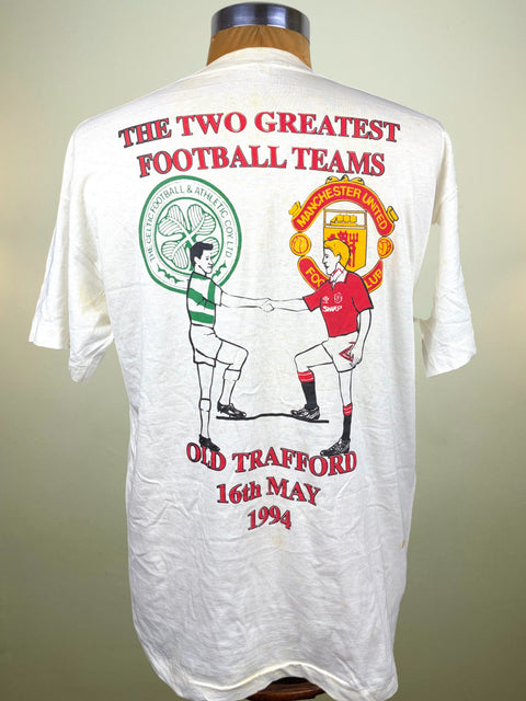 A vintage white graphic t-shirt displayed on a wooden mannequin torso, showing the back print with Celtic and Manchester United football club logos and text celebrating Old Trafford from 1994.