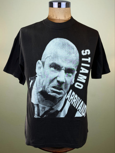 A black short-sleeve graphic T-shirt displayed on a wooden dress form mannequin. The shirt features a large black-and-white portrait print of Gianluca Vialli's face on the front, with the words 'STIAMO ARRIVANDO' printed vertically in white along the right side.