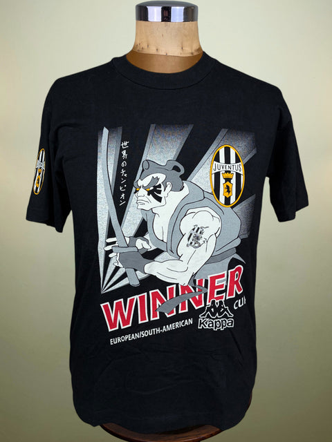 A black short-sleeve graphic T-shirt displayed on a wooden mannequin torso against a plain light background. The shirt features a large front print with a stylized bear, the Juventus crest, Japanese text, and the word 'WINNER' in red, along with Kappa branding.