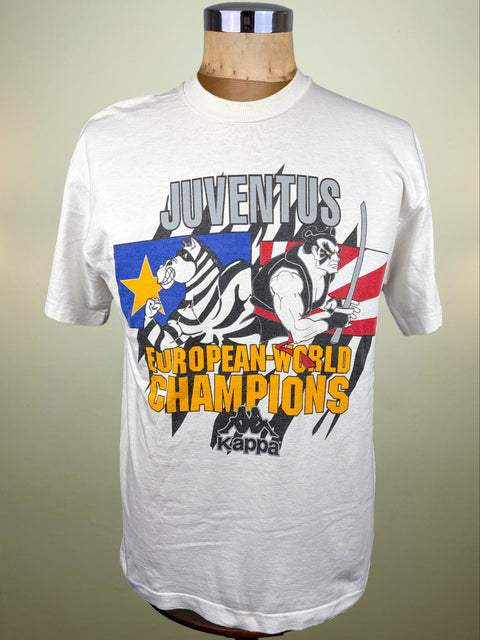 A white short-sleeve graphic T-shirt displayed on a mannequin torso against a plain light background. The shirt features a large front print with the word 'JUVENTUS' in gray, a zebra and muscular figure in black-and-white and red-and-blue flag styling, and bold yellow text reading 'EUROPEAN-WORLD CHAMPIONS.