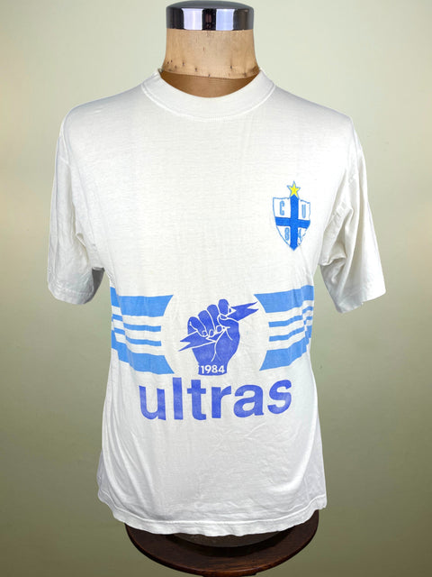 White t-shirt with blue graphics and text on a mannequin against a beige background