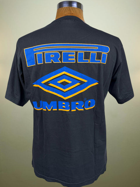 A dark charcoal gray short-sleeve t-shirt displayed on a mannequin torso, showing the back with a large blue and yellow Umbro Pirelli logo graphic.