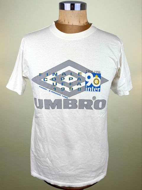 A vintage white Umbro t-shirt displayed on a wooden dress form mannequin. The shirt features a large graphic print for the 1998 UEFA Cup Final in Paris, with the Umbro logo and 'FINALE COPPA UEFA 1998' text.