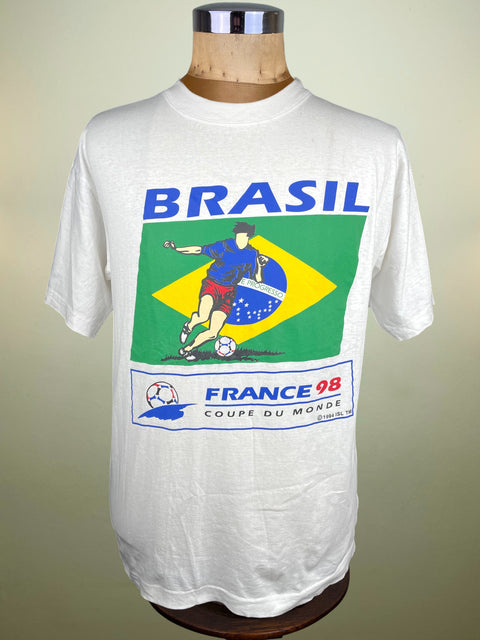 White t-shirt with 'Brasil' and soccer design on a mannequin against a beige background