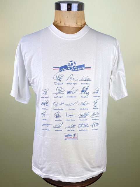 White t-shirt with blue graphics and signatures on a mannequin against a beige background