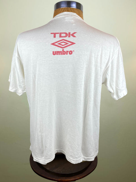 White t-shirt with TDK and Umbro logos on a mannequin against a beige background