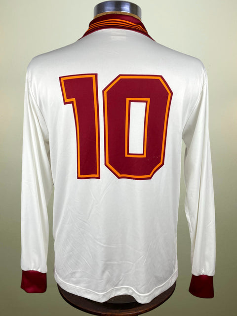White AS Roma jersey with red number 10 on a mannequin against a beige background