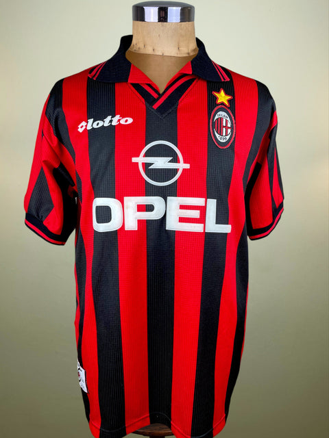 Red and black AC Milan 1997-98 striped sports jersey with Opel and Lotto brand logos on a mannequin against a beige background.