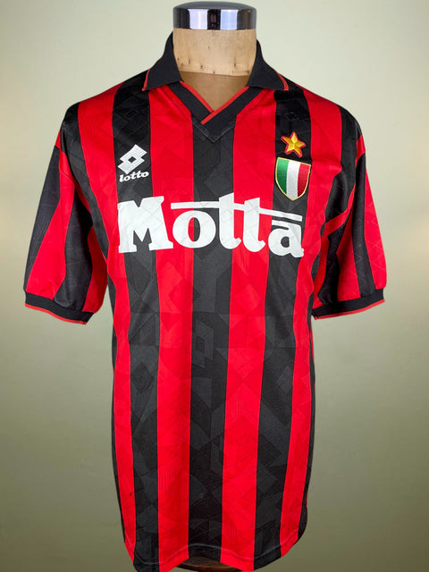Red and black striped Lotto AC Milan Home jersey with Motta branding on a mannequin against a neutral background