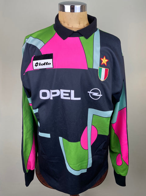 A short-sleeved soccer jersey featuring a geometric pattern with pink, green, and black colors, and the logos of AC Milan and Opel.