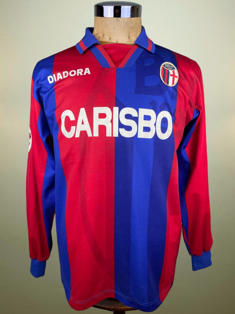 A long-sleeved Bologna 1996-97 home jersey with Carisbo sponsor, predominantly red with blue and white accents, and the crest of a football club.