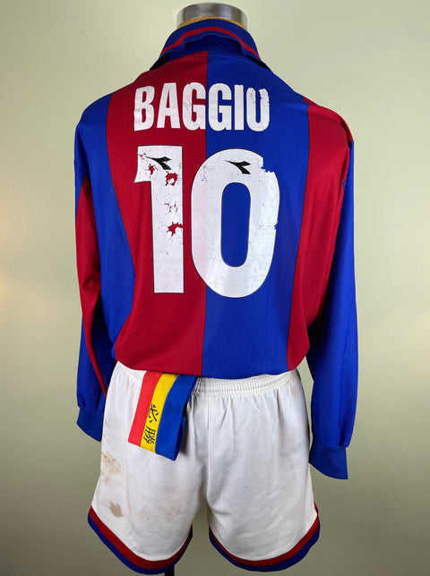 A long-sleeved Bologna 1997-98 jersey with 'Baggio 10' printed on the back, predominantly red with blue details and a yellow badge on the right sleeve, accompanied by a white soccer shorts with a colorful badge on the left leg.