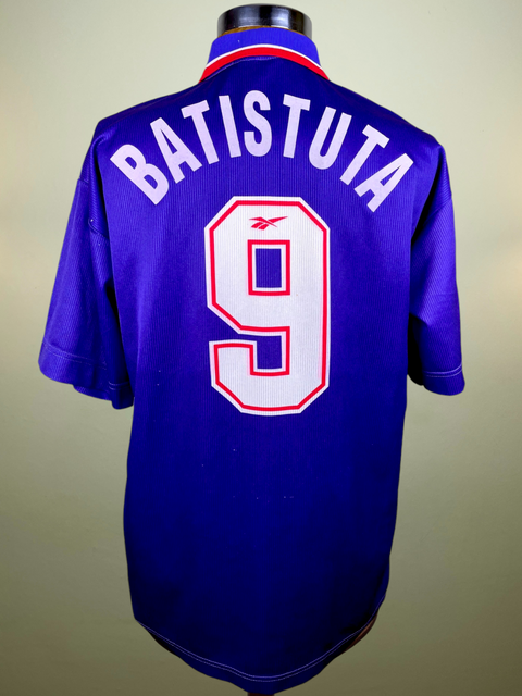 A short-sleeved Fiorentina 1996-97 jersey with the name 'BATISTUTA' printed on the back in red and white colors, with a V-neck collar.