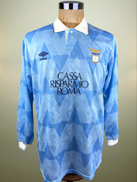 A blue long-sleeved soccer Lazio 1989 home Jersey on a mannequin, featuring geometric patterns and the sponsor 'CASSA RISPARMIO ROMA' on the front.