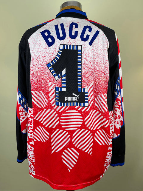 A vintage Puma soccer jersey shown from the back on a mannequin, featuring 'BUCCI' and the number '1' in blue and white, with a red, white, and black patterned design.