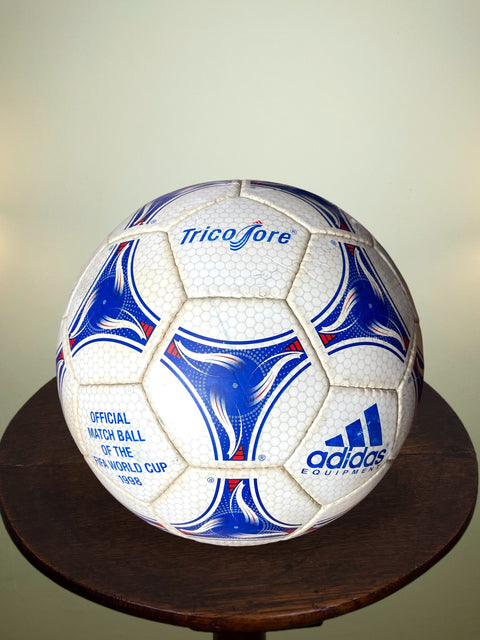 White soccer ball with blue and red patterns on a wooden stand against a light background