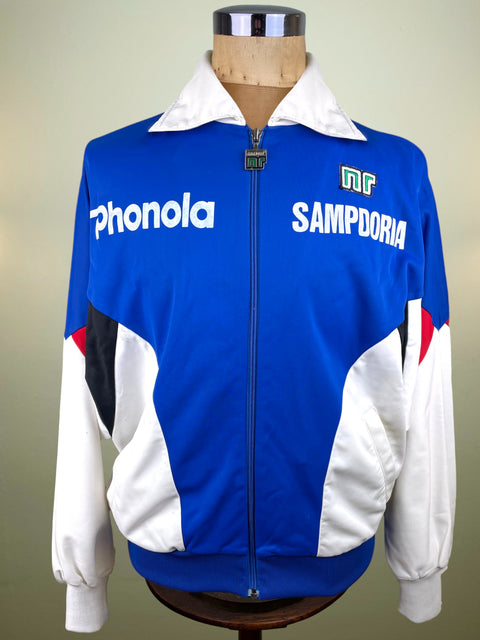 A vintage blue, white, and black track jacket displayed on a mannequin. The jacket features 'Phonola' and 'SAMPDORIA' text on the chest, with a blue front zipper, white collar, and white, black, and red color-blocked panels on the sleeves and sides.
