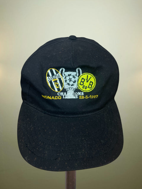 Black cap with embroidered design from the 1997 Champions League Final - Juventus vs Borussia Dortmund and the details of the final on a beige background