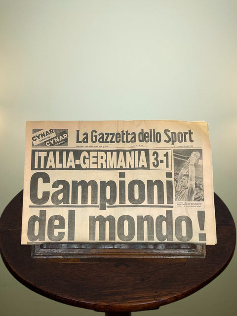 Vintage newspaper titled 'La Gazzetta dello Sport' Celebrating Italy's 1982 World Cup win on a wooden stand with a light background