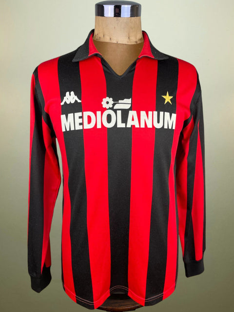 A red and black striped AC Milan soccer jersey from the 1987 season, with Mediolanum sponsor on the chest, displayed on a mannequin.