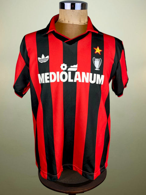 A red and black striped AC Milan Adidas soccer jersey from 1990, displayed on a mannequin.