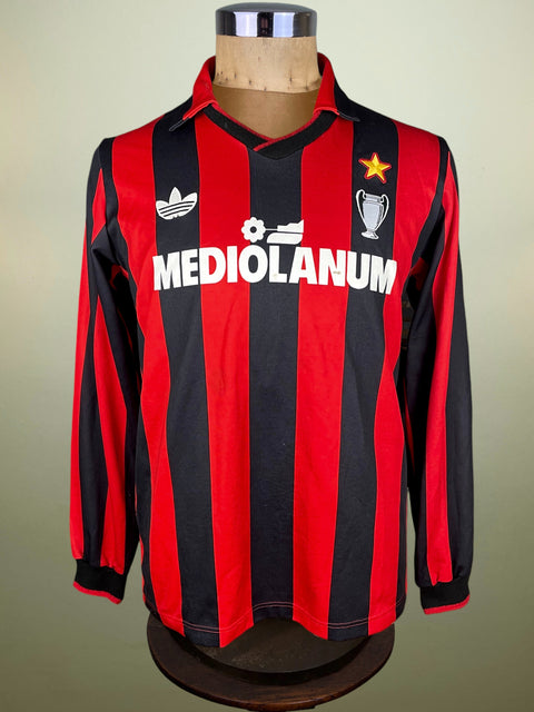 Red and black striped AC Milan 1990 jersey with Mediolanum branding and made by Adidas with the logo on the chest on a mannequin against a beige background