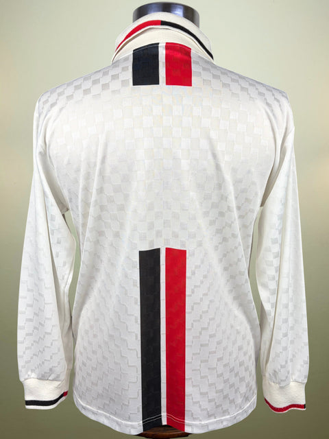 A white long-sleeve soccer jersey with a subtle checkered pattern, featuring vertical red and black stripes on the back and collar, displayed on a mannequin.