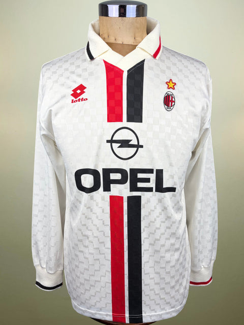 A vintage 1995-1996 AC Milan long-sleeve soccer jersey by Lotto, featuring a white textured pattern, red and black vertical stripes, and a large black Opel sponsor logo on the front, displayed on a wooden mannequin torso.