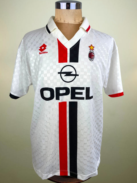 A vintage AC Milan football jersey by Lotto, featuring a white textured pattern with red and black vertical stripes, displayed on a wooden mannequin torso against a beige background.