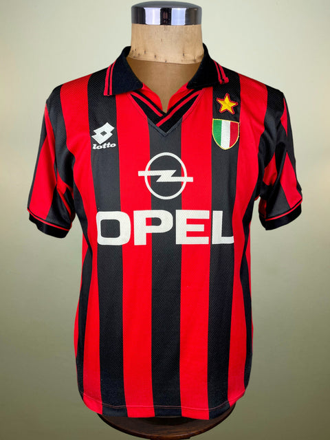A vintage AC Milan soccer jersey with red and black vertical stripes, featuring the white Opel sponsor logo, Lotto brand logo, and Italian club crest, displayed on a wooden mannequin torso.