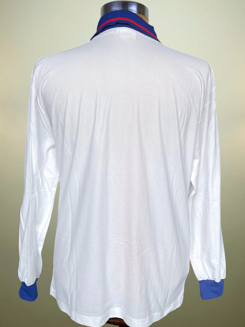 A white long-sleeve collared shirt shown from the back on a mannequin, with blue cuffs and a blue and red striped collar.