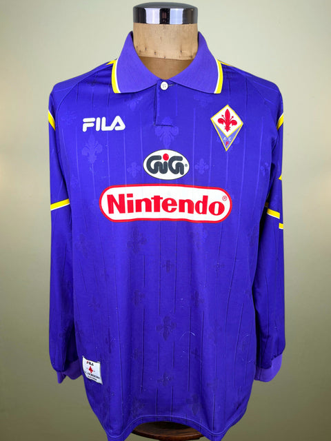 A vintage 1997-1998 Fiorentina home soccer jersey by Fila, featuring a royal blue body with yellow piping, the club crest, and sponsor logos including Nintendo and GiG, displayed on a wooden mannequin torso.