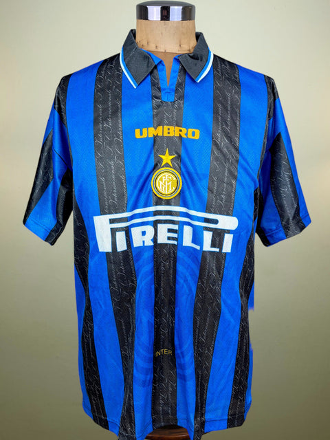 A vintage Inter Milan home soccer jersey by Umbro, featuring blue and black vertical stripes with a subtle script pattern, displayed on a wooden mannequin torso. The jersey has the Inter Milan club crest in the center, the Pirelli sponsor logo in white across the chest, and the Umbro brand logo in yellow above it.